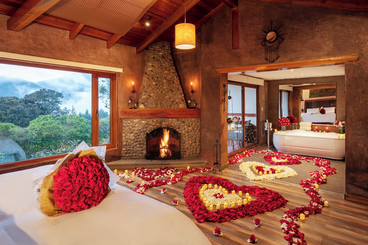 A room with a stone fireplace, a bed with rose petals and candles, and a view of the outdoors.
