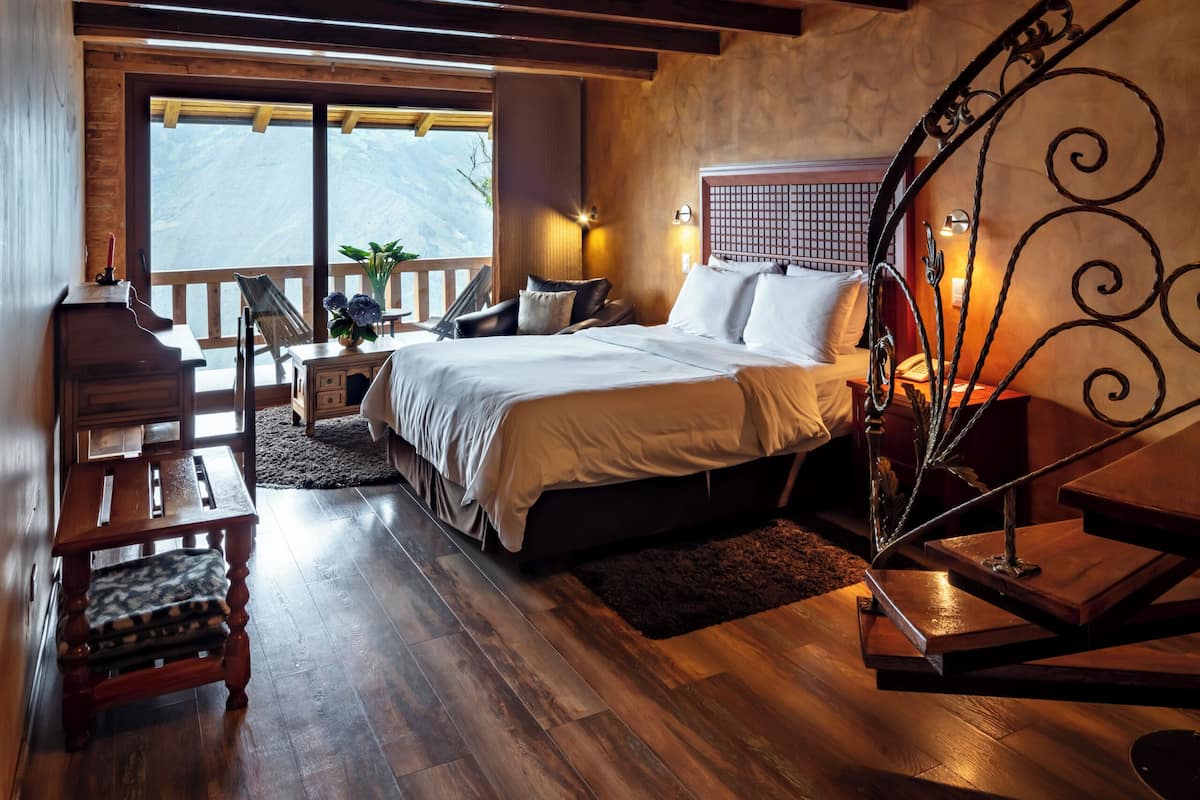 A bedroom with a wooden ceiling, a bed, a nightstand, and a window with a view.