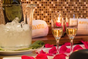 Una botella de champán, dos copas, hielo y pétalos de rosa sobre una mesa.