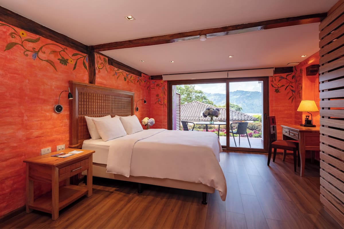 A bedroom with a bed, wooden nightstands, a desk, and a view of the outdoors.