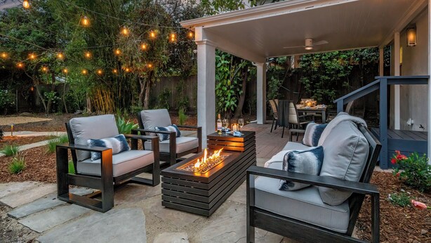 An outdoor patio with a fire pit, seating area, and string lights.