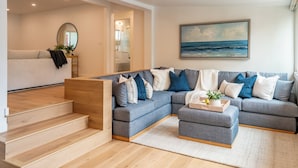 A modern living room with a grey sectional sofa, a coffee table with a tray and plant, and a staircase leading to an upper level.