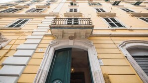 Une façade d’immeuble avec une entrée centrale, de nombreuses fenêtres et un balcon doté de rampes en métal.