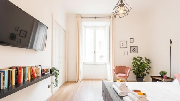 Une chambre d’hôtel moderne, équipée d’un lit, d’un téléviseur fixé au mur, d’une table de chevet, d’une chaise et d’une plante en pot.
