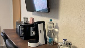 A hotel room with a flat-screen TV mounted on the wall, a coffee maker, a water bottle, and a glass container on the counter. - Apartments & Zimmer (Vettweiß)