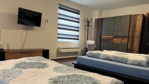 A bedroom with two beds, a TV, a heater, and a window with blinds. - Apartments & Zimmer (Vettweiß)