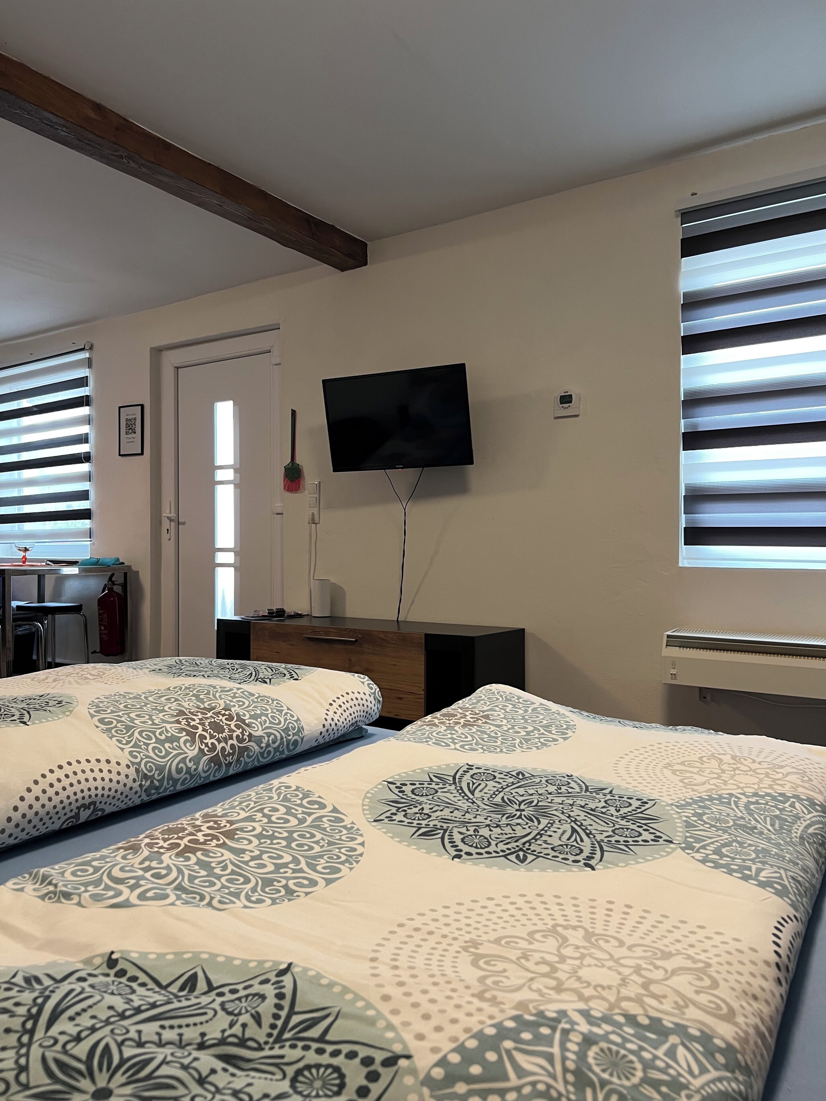 Ett hotellrum med två sängar, en tv som är monterad på väggen, ett skrivbord med en stol och ett fönster med persienner.