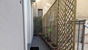 A narrow outdoor corridor with tiled flooring, potted cacti, and a wooden lattice fence.