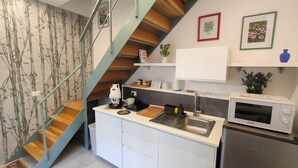 A compact kitchen with a built-in microwave, a coffee maker, and a sink. There's a staircase with wooden steps and a metal railing.
