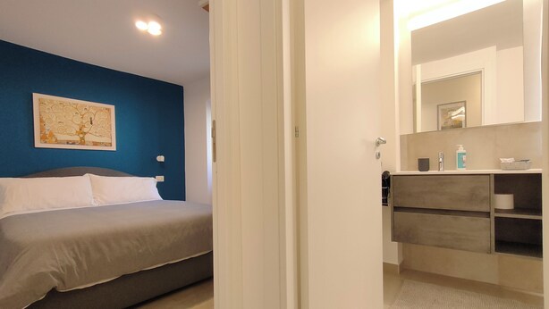 A bedroom with a bed, a nightstand, a mirror, and a bathroom with a sink and storage.