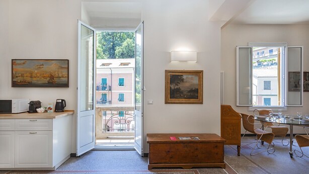 Un espacio habitable pequeño con kitchenette, comedor y vista a la calle por una puerta abierta.