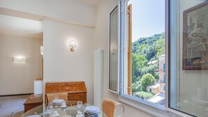 Un comedor con una mesa de vidrio preparada para cuatro, un aparador de madera y un ventanal con vistas a una colina.