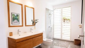 Un baño moderno con tocador de madera, dos espejos, un inodoro y zona de ducha.