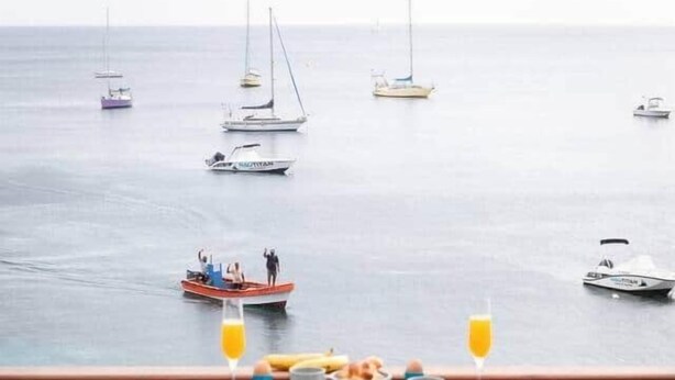 Una mesa de desayuno con comidas y dos sillas en un balcón con vista al mar y barcos.