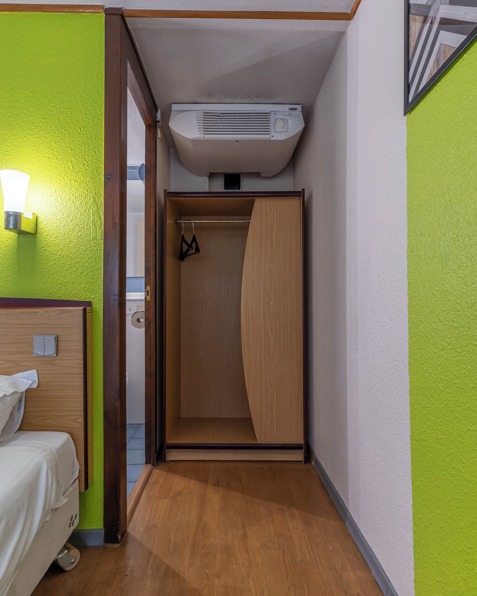 Une chambre d’hôtel avec un lit, une armoire en bois, un mur vert et un appareil de climatisation.