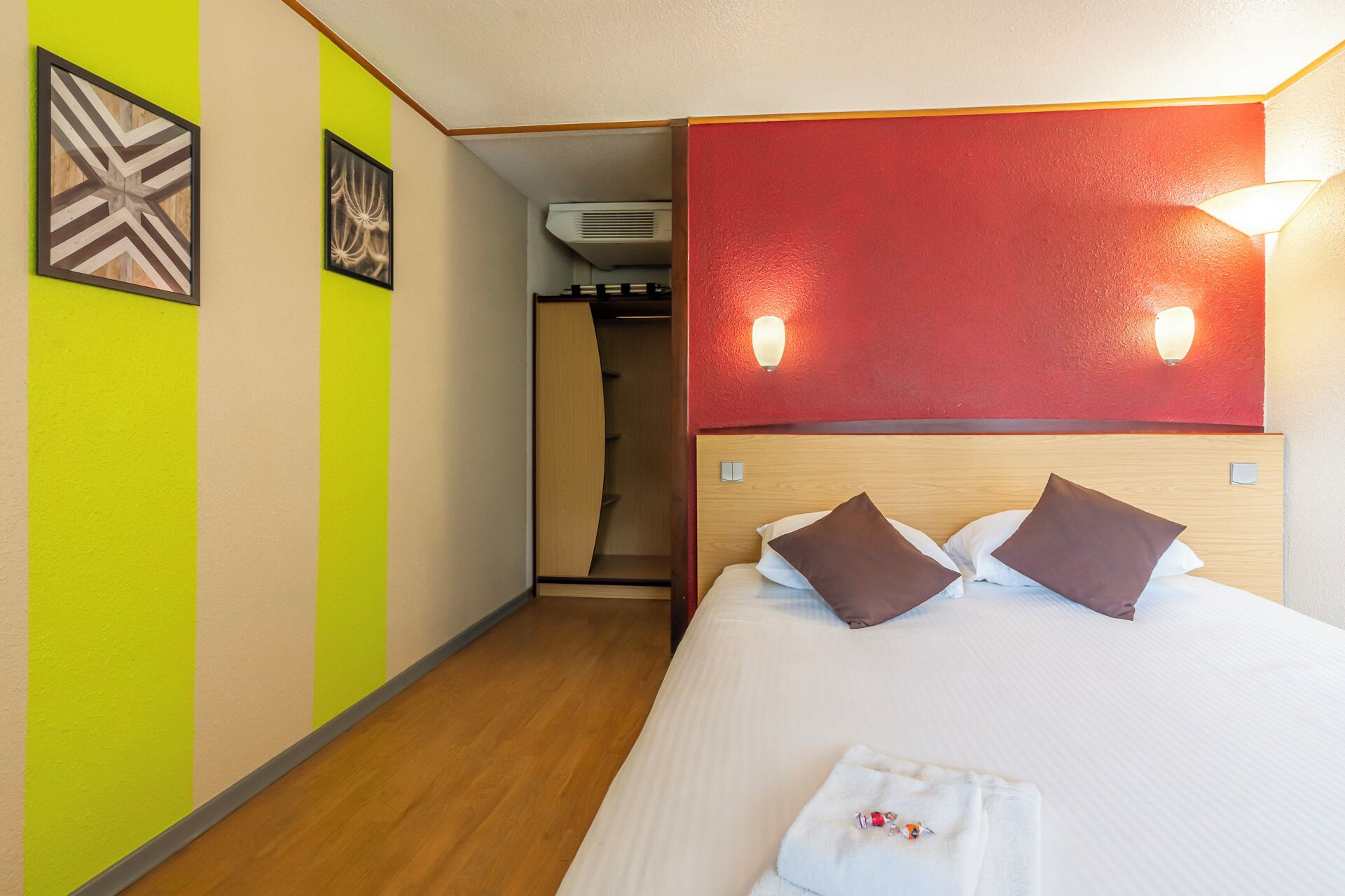 A hotel room with a bed, a red accent wall, and two wall-mounted lights.