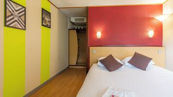 A hotel room with a bed, a red accent wall, and two wall-mounted lights.