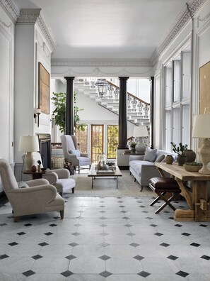 Un salón amplio con techos altos, ventanas grandes y una escalera que sube a un piso superior.