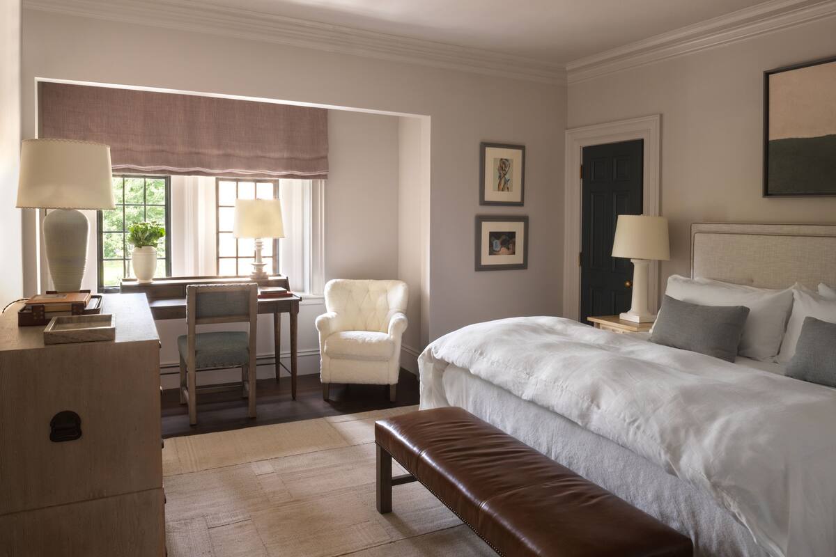 Una habitación de hotel con una cama, un escritorio con una silla, un banco y dos lámparas.