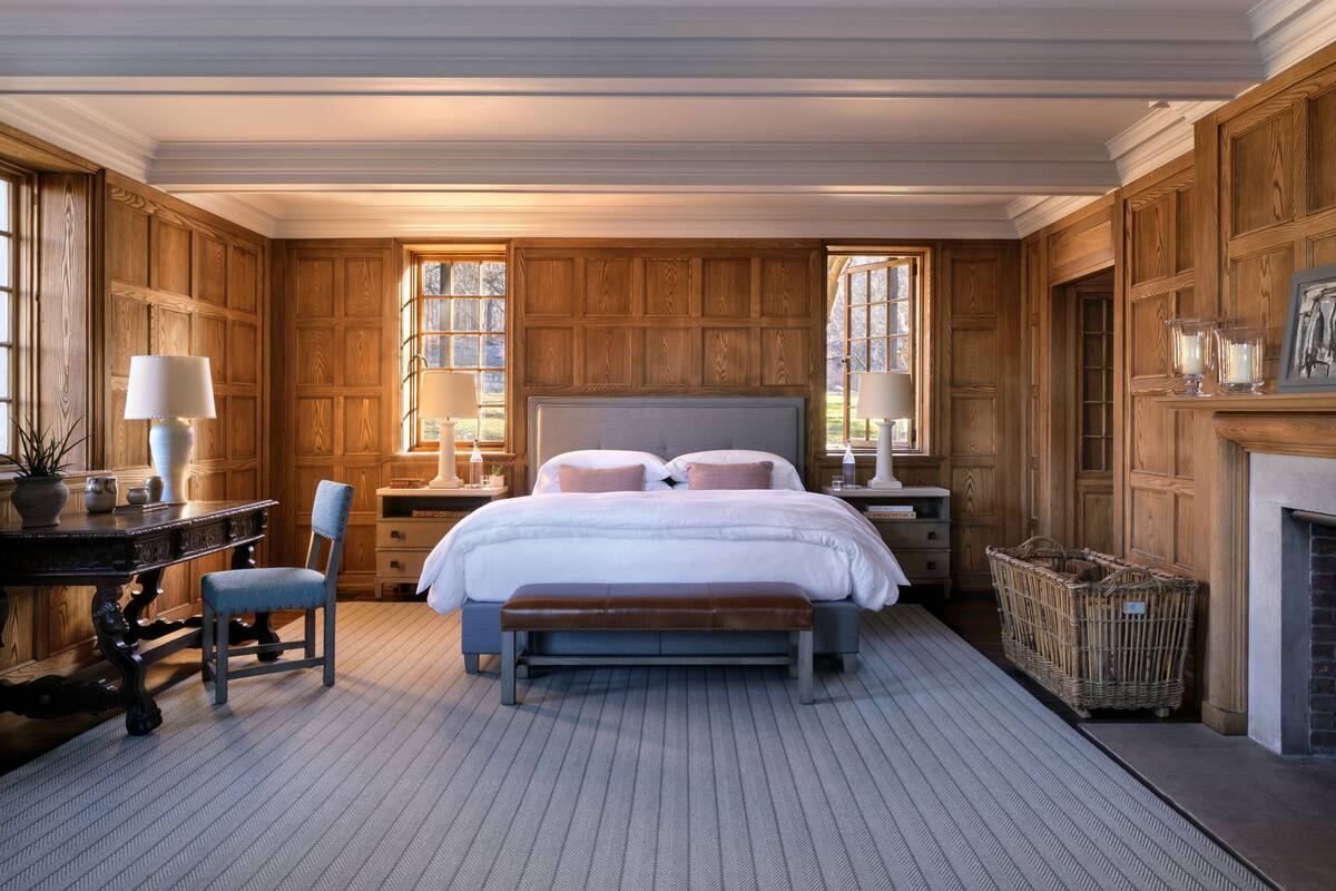 Un dormitorio con una cama grande, paredes de paneles de madera, un escritorio con silla y una chimenea.
