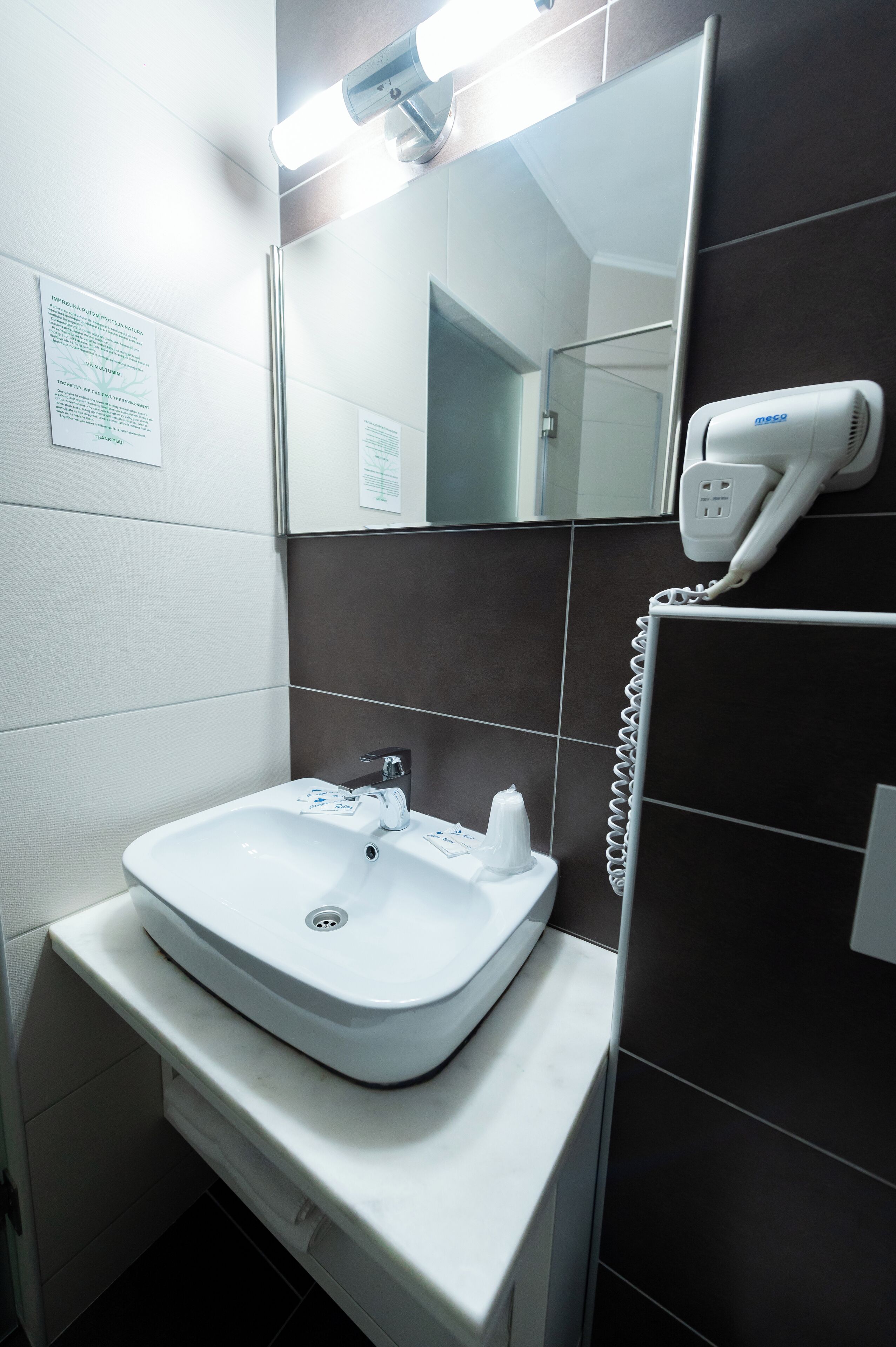 A bathroom with a white sink, a mirror, and a hairdryer on the wall.