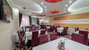 A restaurant with multiple tables and chairs, a television mounted on the wall, and a patterned carpet. - Complex Turistic Monaco (Baile Felix)