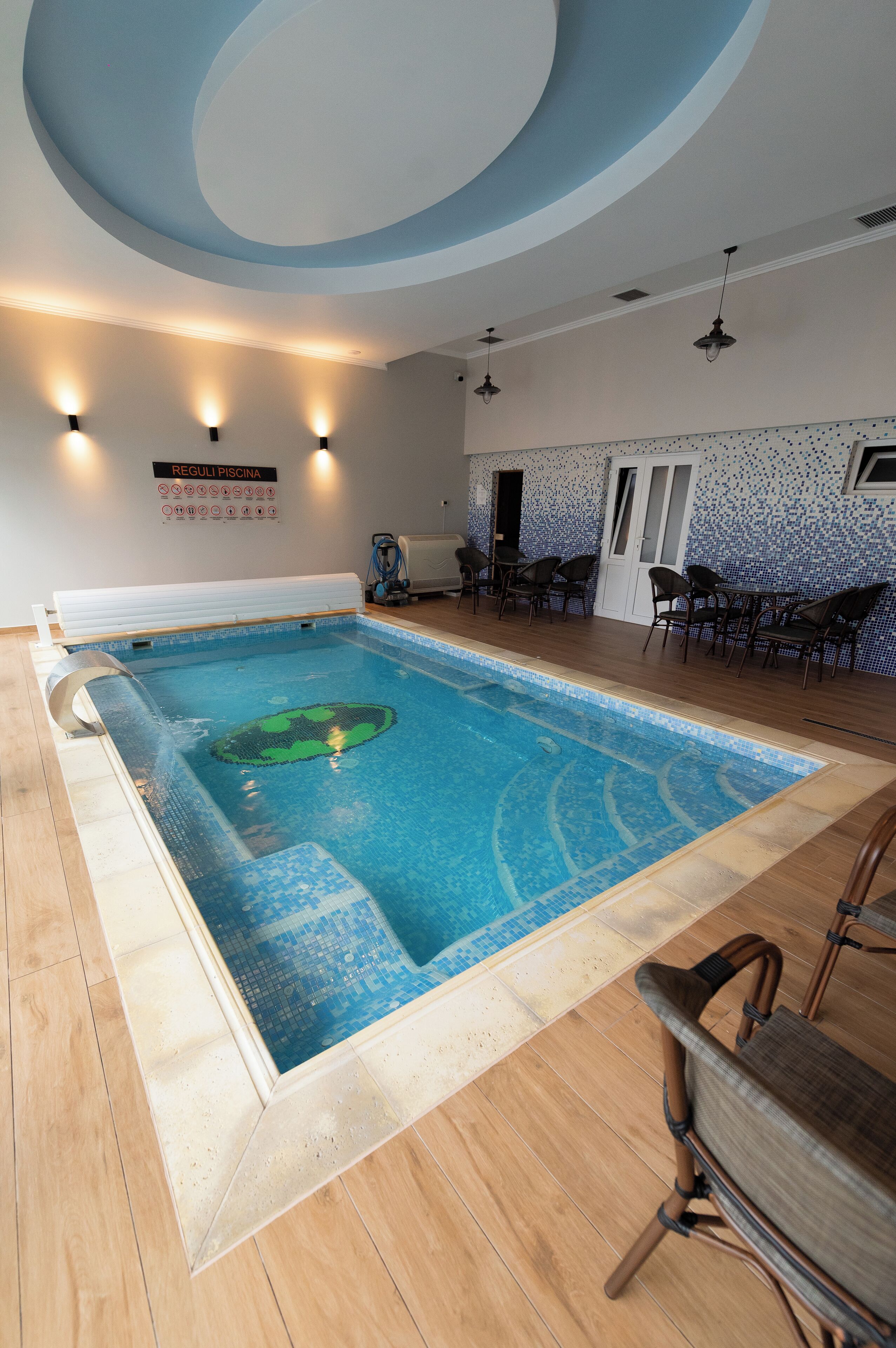 A swimming pool with a tiled floor, surrounded by chairs and a sign indicating pool rules.