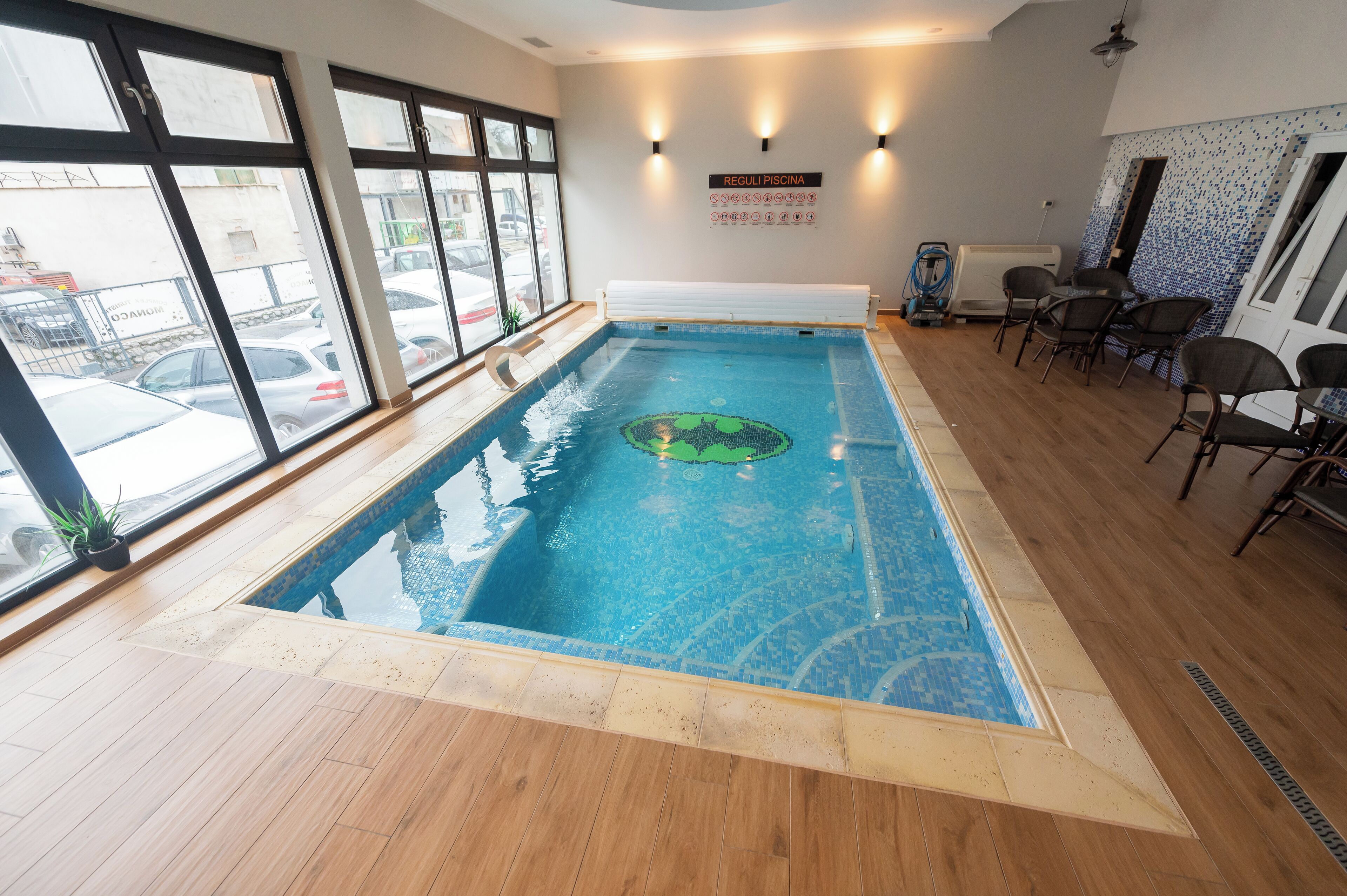An indoor swimming pool with a tiled floor, a green inflatable ring, and a sign indicating pool rules.
