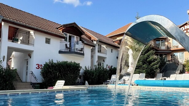 A swimming pool with clear blue water, surrounded by a building with balconies and a tiled roof. - Complex Turistic Monaco (Baile Felix)