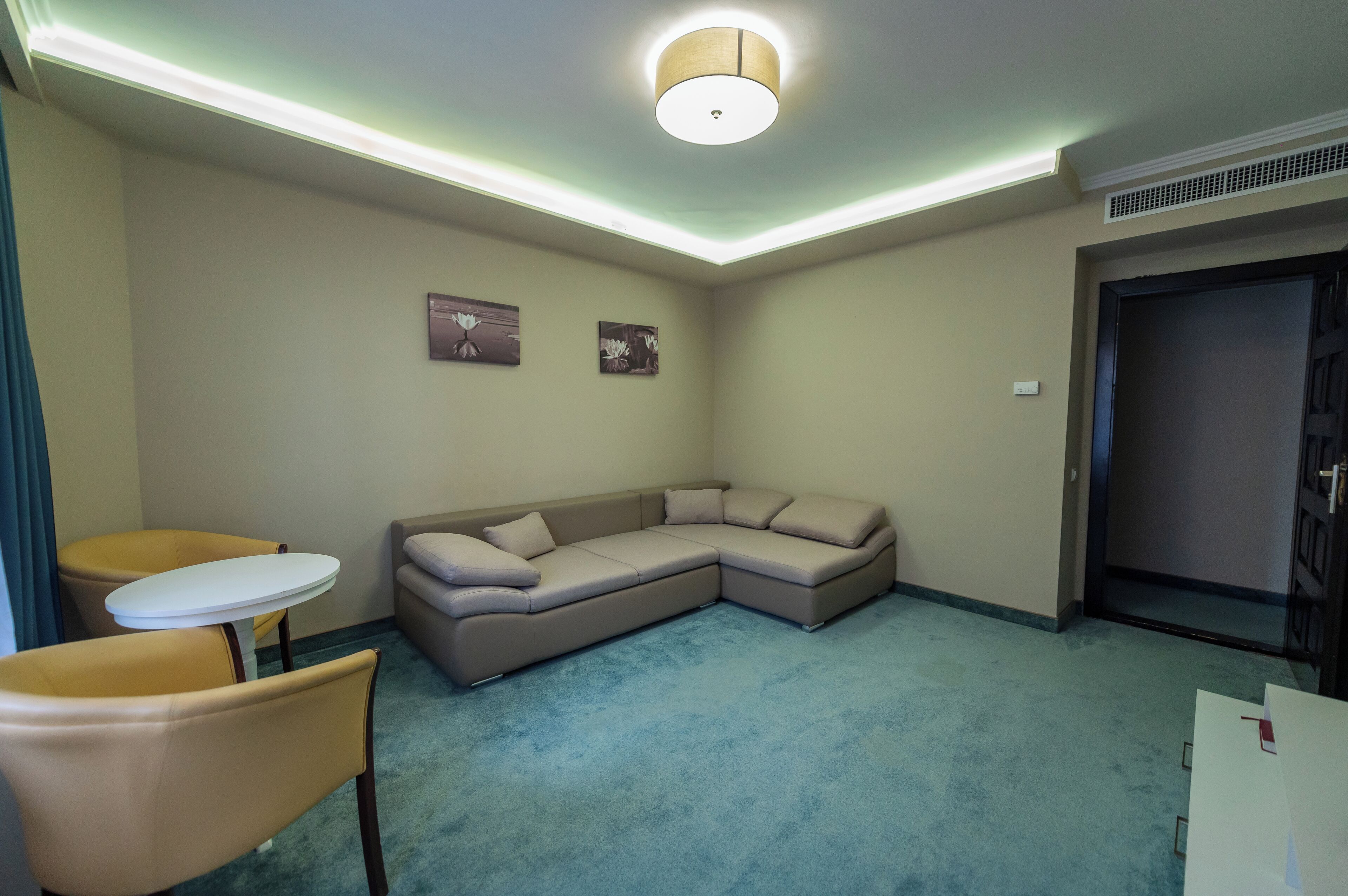 A room with a beige sectional sofa, a small round table, and two chairs.