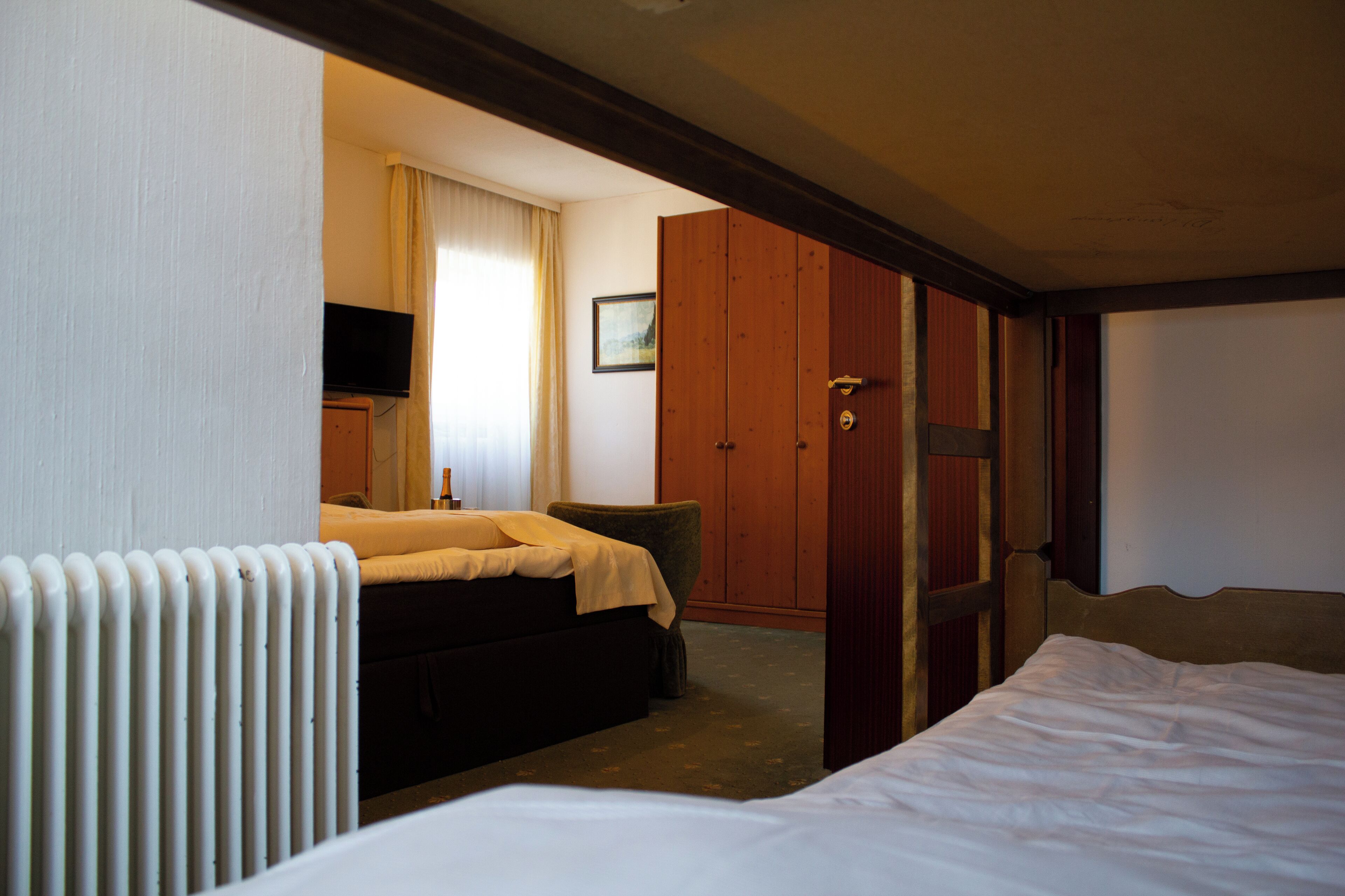 A hotel room with a bed, a chair, a television, a wardrobe, and a radiator.