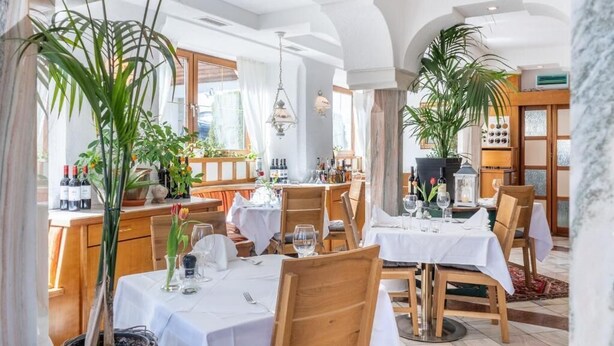 Un restaurante con mesas dispuestas para comer, plantas en macetas y botellas de vino en estantes.