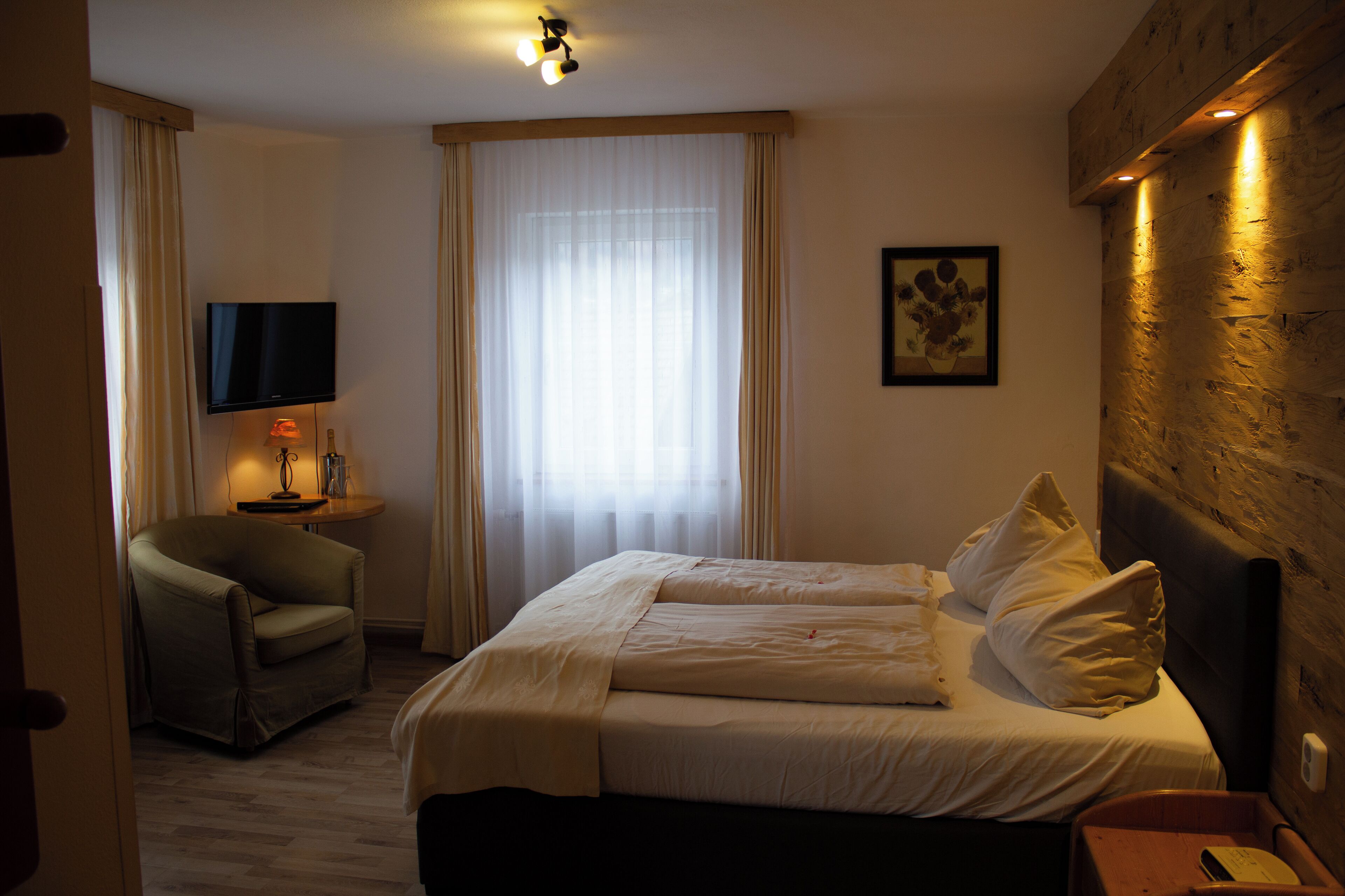 Une chambre d’hôtel avec un lit, une chaise, une télévision et une fenêtre avec des rideaux.