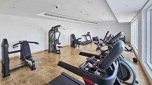 Une salle de sport équipée de divers appareils d’exercice, notamment des tapis de course et des appareils de musculation, avec une grande fenêtre sur l’un des murs.