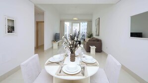Un espace repas moderne avec une table ronde dressée pour quatre personnes, un vase de fleurs et un canapé en arrière-plan.