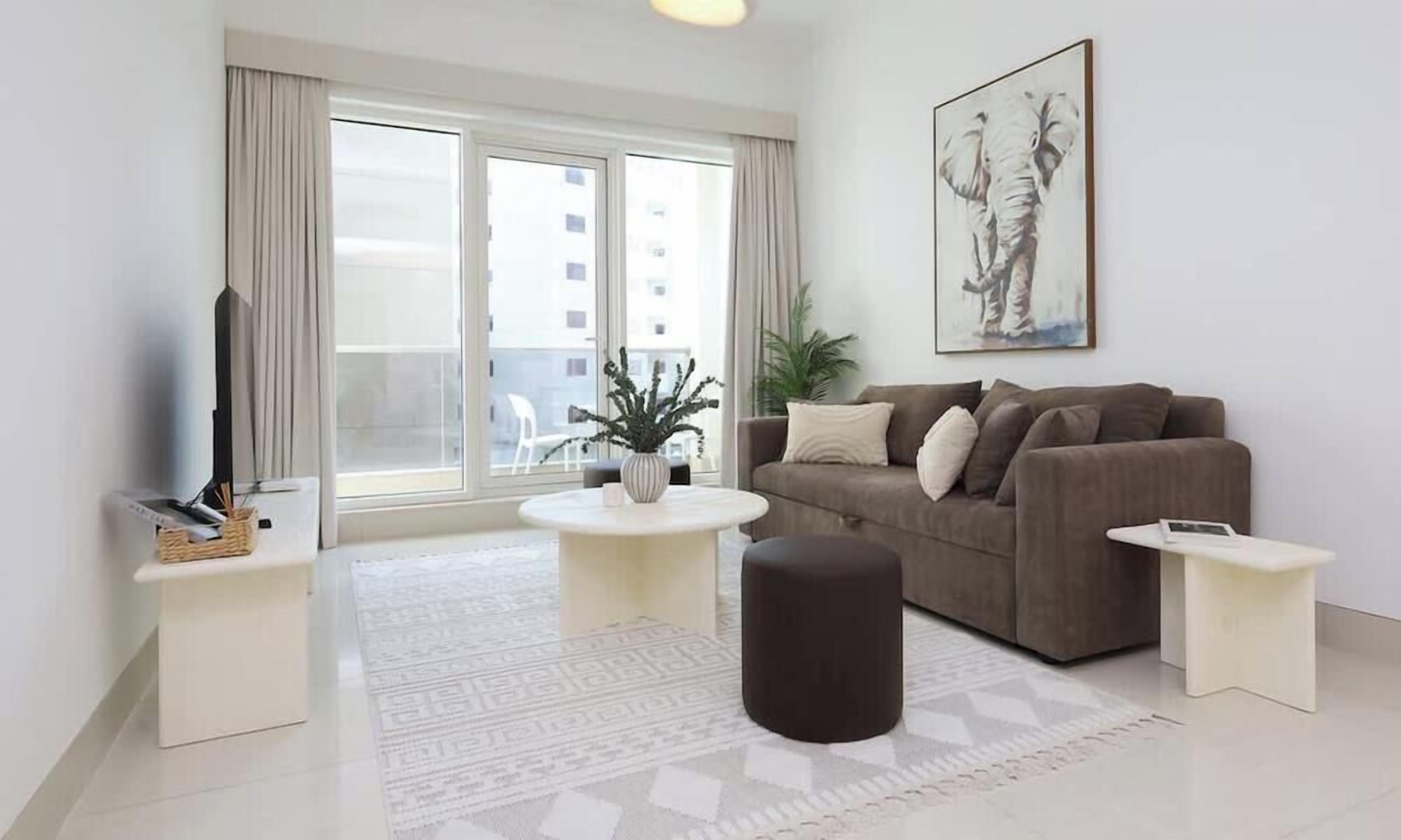 Un salon moderne comprenant un canapé, une table basse, un pouf et un téléviseur à écran plat.