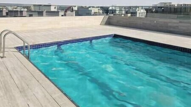 A rooftop swimming pool with a wooden deck and a metal handrail. - Luxury Apt W Pool Near Airport & Downtown Dubai (Dubai)