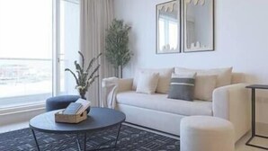 A modern living room with a sofa, a round coffee table, and a potted plant. - Luxury Apt W Pool Near Airport & Downtown Dubai (Dubai)