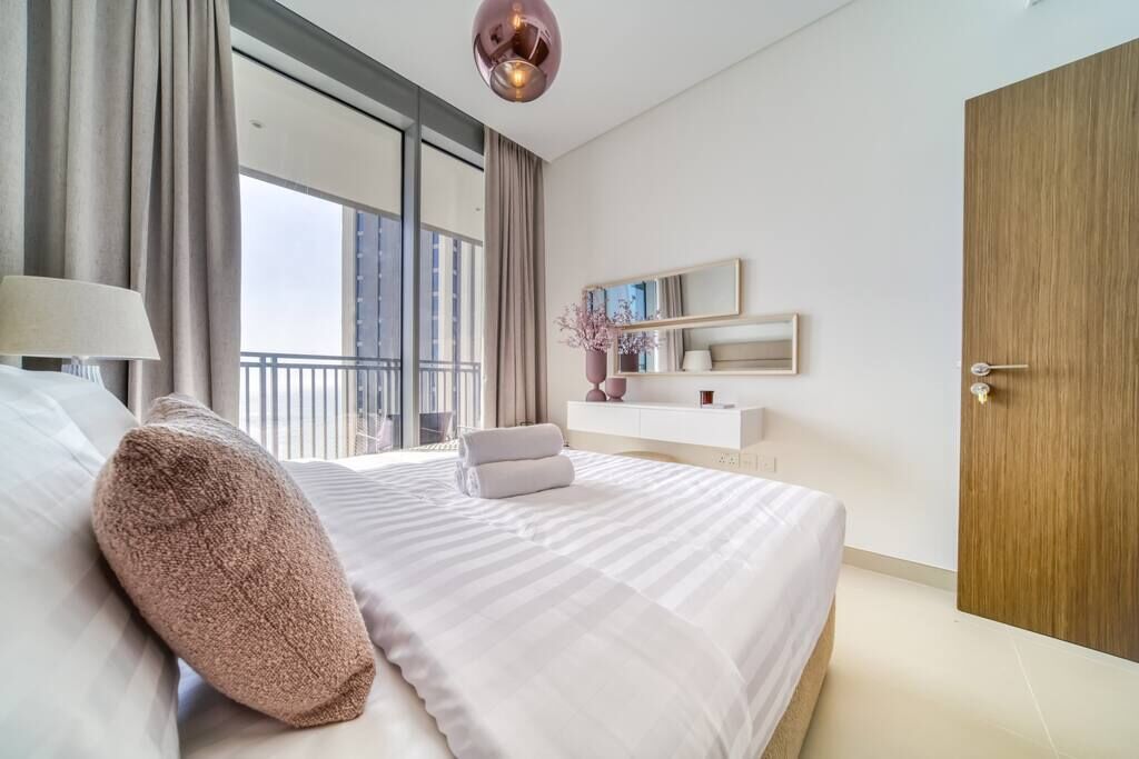 Ein modernes Hotelzimmer mit einem großen Bett, einer Nachttischlampe, einer Holztür, einem Balkon mit Blick und einem kleinen Tisch mit Stuhl.