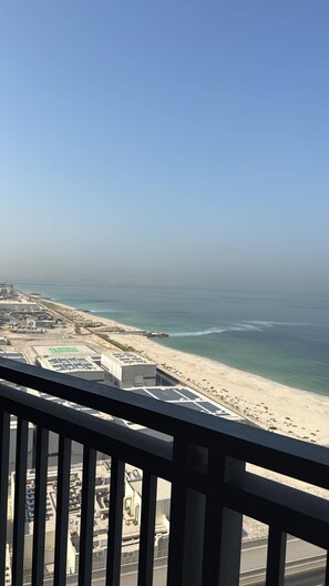 A coastal view from a balcony with a clear sky, a sandy beach, and a calm sea.