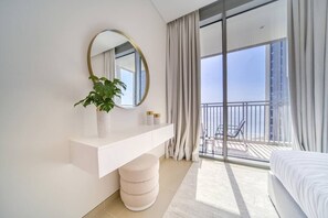 A modern bedroom with a large window, a round mirror, a bedside plant, and a white bed. - Bluewaters Oceanview Apt w/ Infinity Pool & Gym (Dubai)