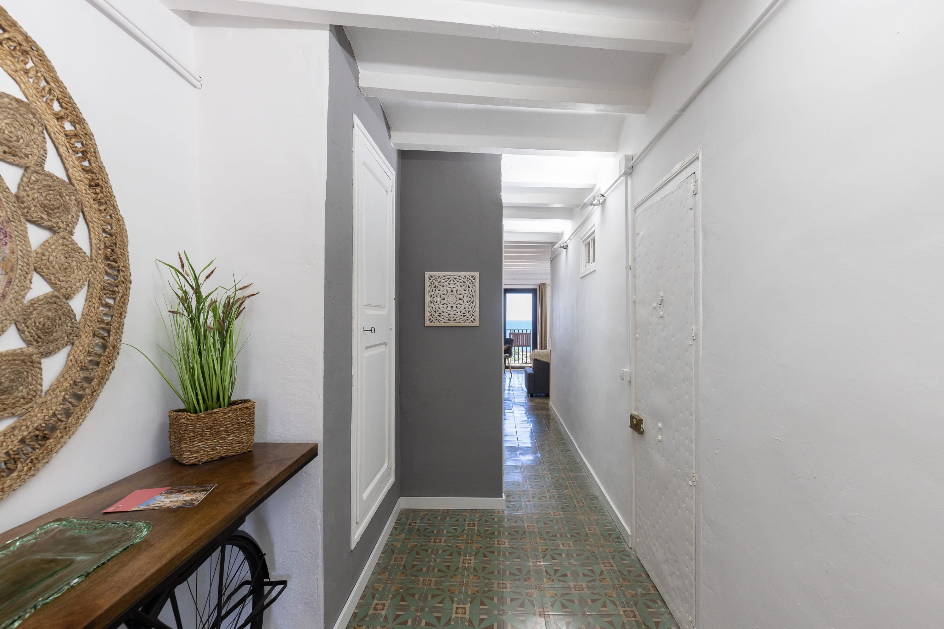 A hallway with a wooden bench, a potted plant, and a decorative wall piece.