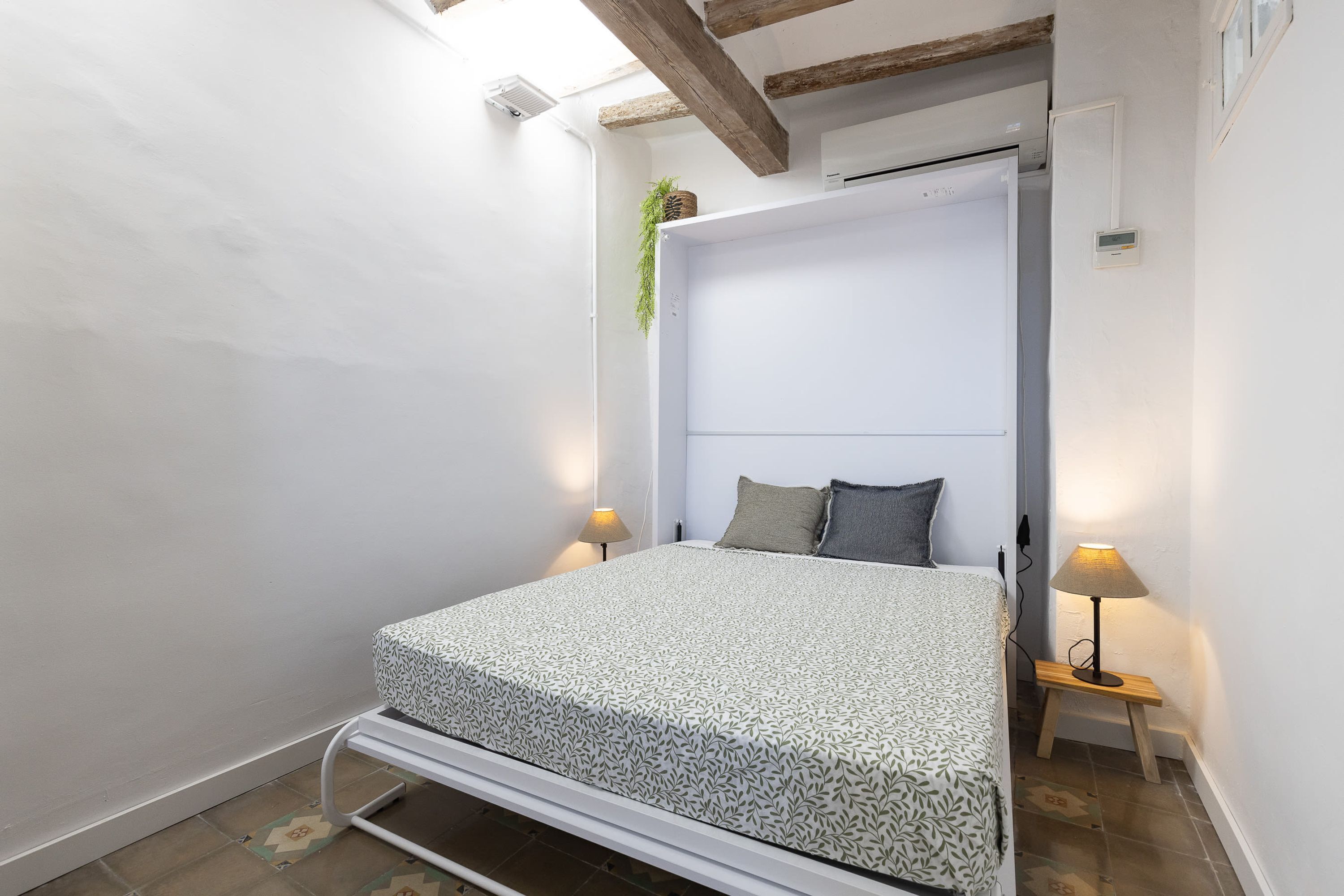 Une petite chambre à coucher, bien éclairée, avec un lit, des lampes de chevet et un ventilateur de plafond.