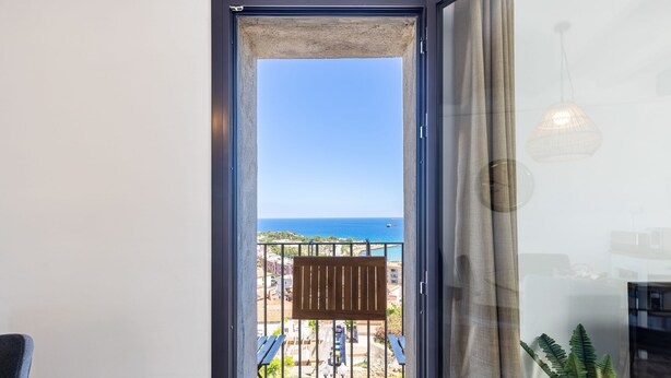 Un balcón con vista al mar, un banco de madera y una lámpara colgante.