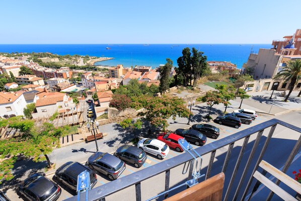 A coastal cityscape with a view of the sea, parked cars, and buildings.