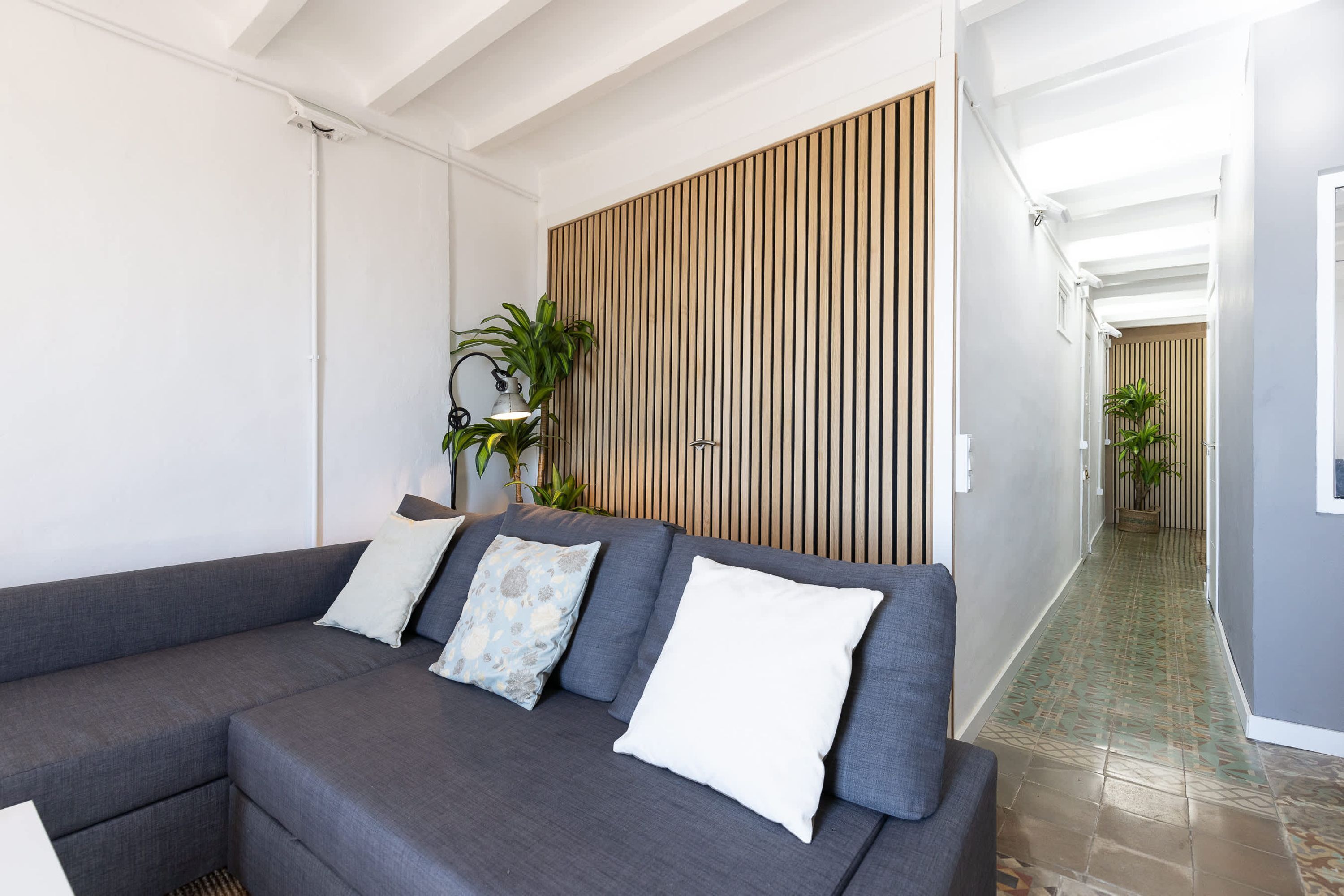 A modern living room with a grey sectional sofa, a wooden slat wall, and a tiled floor.