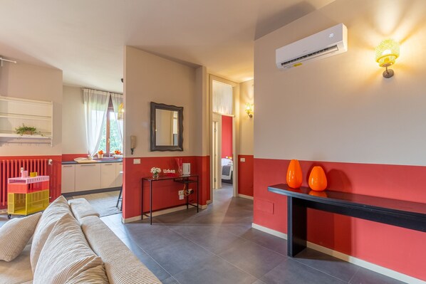 Un salon moderne avec un canapé, un coin repas comprenant une table et des chaises, et une cuisine aux couleurs rouge et blanche.