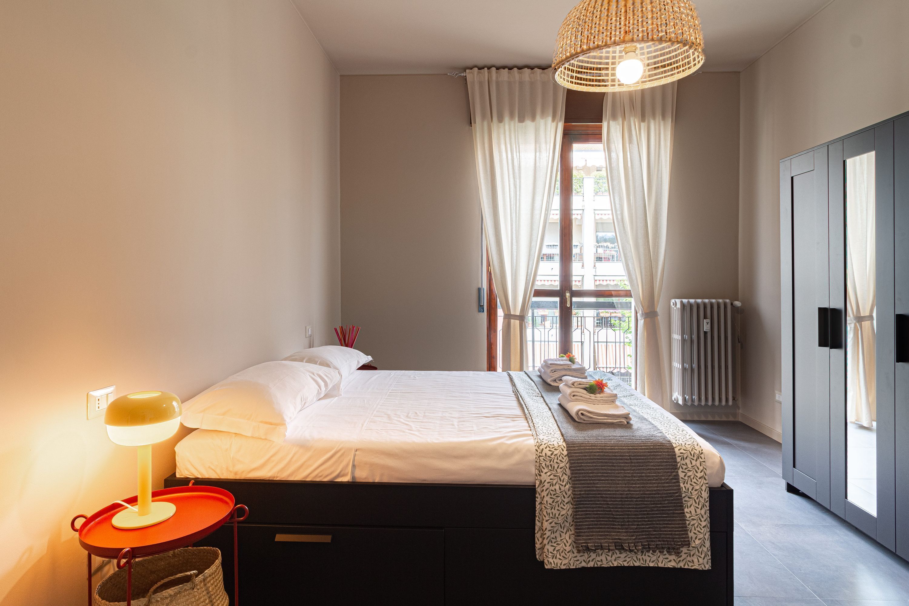Quarto com cama, luminária de cabeceira e vista para o exterior.