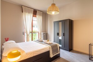 Une chambre à coucher comprenant un lit, une lampe de chevet, une armoire et une fenêtre avec des rideaux.