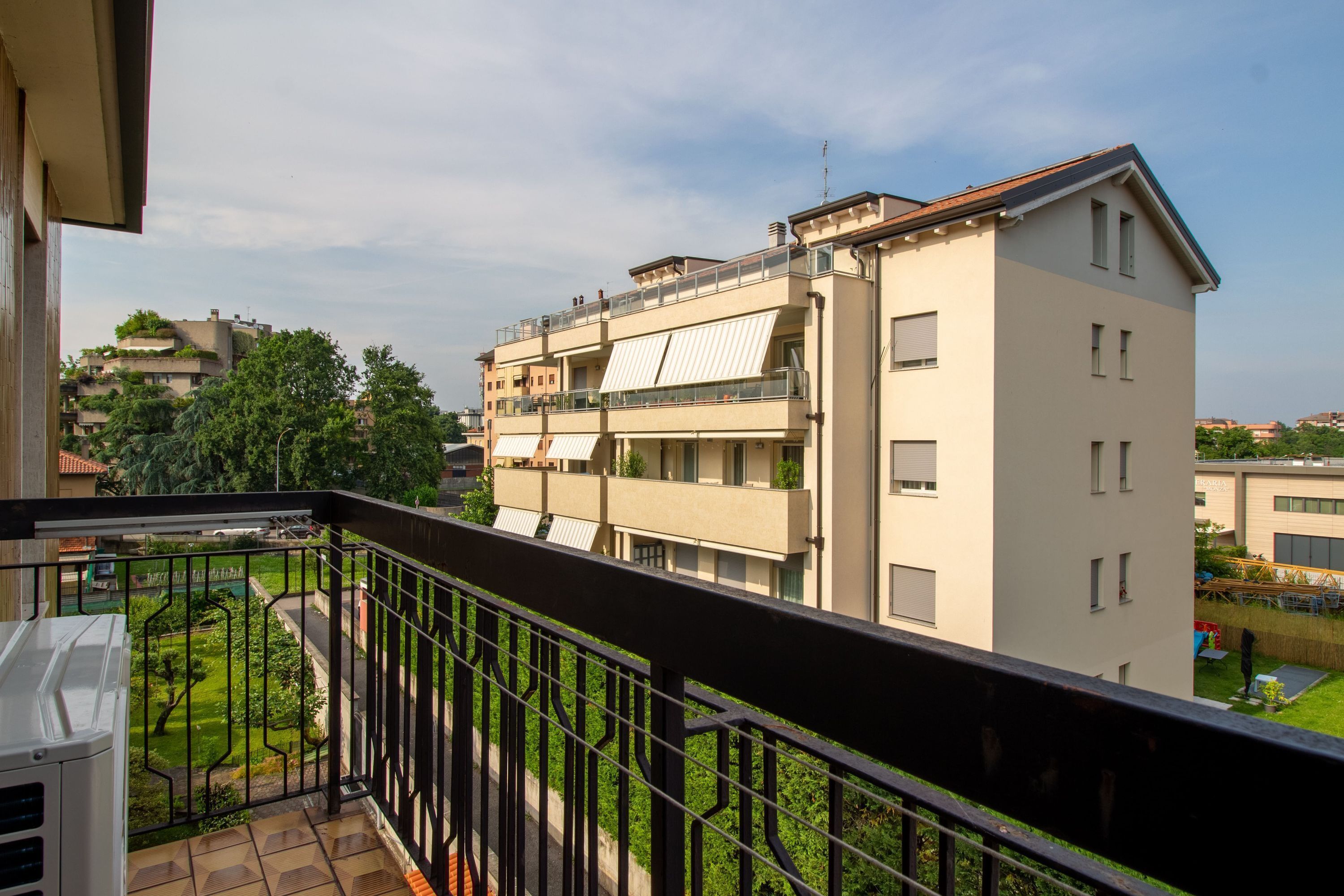 A multi-story residential building with balconies, a garden area, and a clear sky.